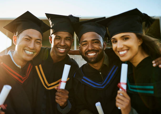 Portrait of diverse group of unicaf online scholarship graduates holding degree and diploma during graduation ceremony outside on university campus. Smiling and happy friends standing close together at college